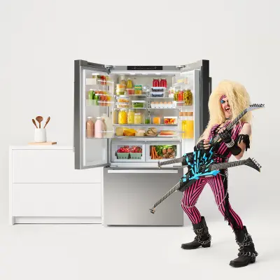 A Bosch 800 Series French-Door Refrigerator is highlighted alongside a classic 70s rockstar. The rocker, dressed in colorful clothes with wild blonde hair, passionately plays an electric guitar, creating an edgy and innovative atmosphere.